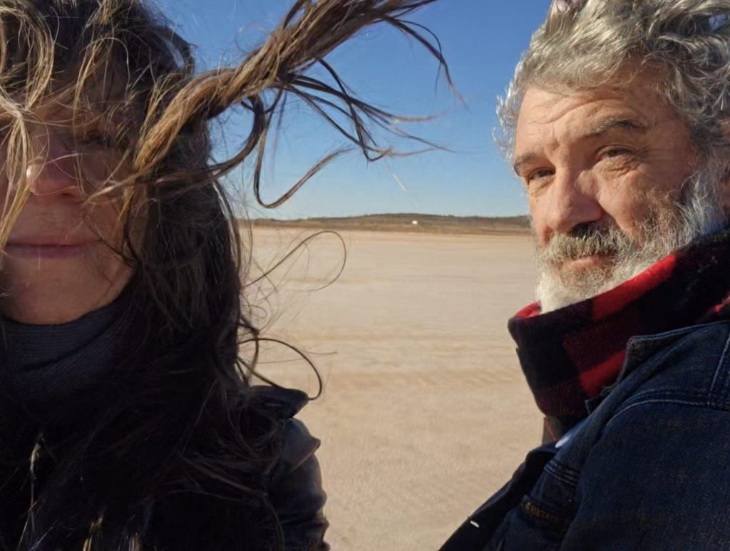 Two people in windy desert landscape.
