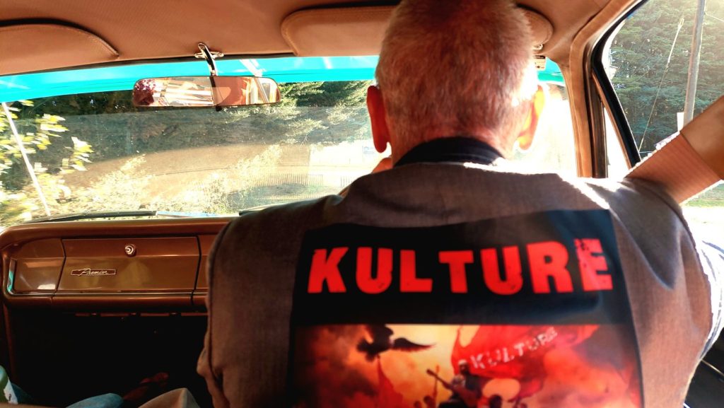 Man driving car wearing KULTURE shirt