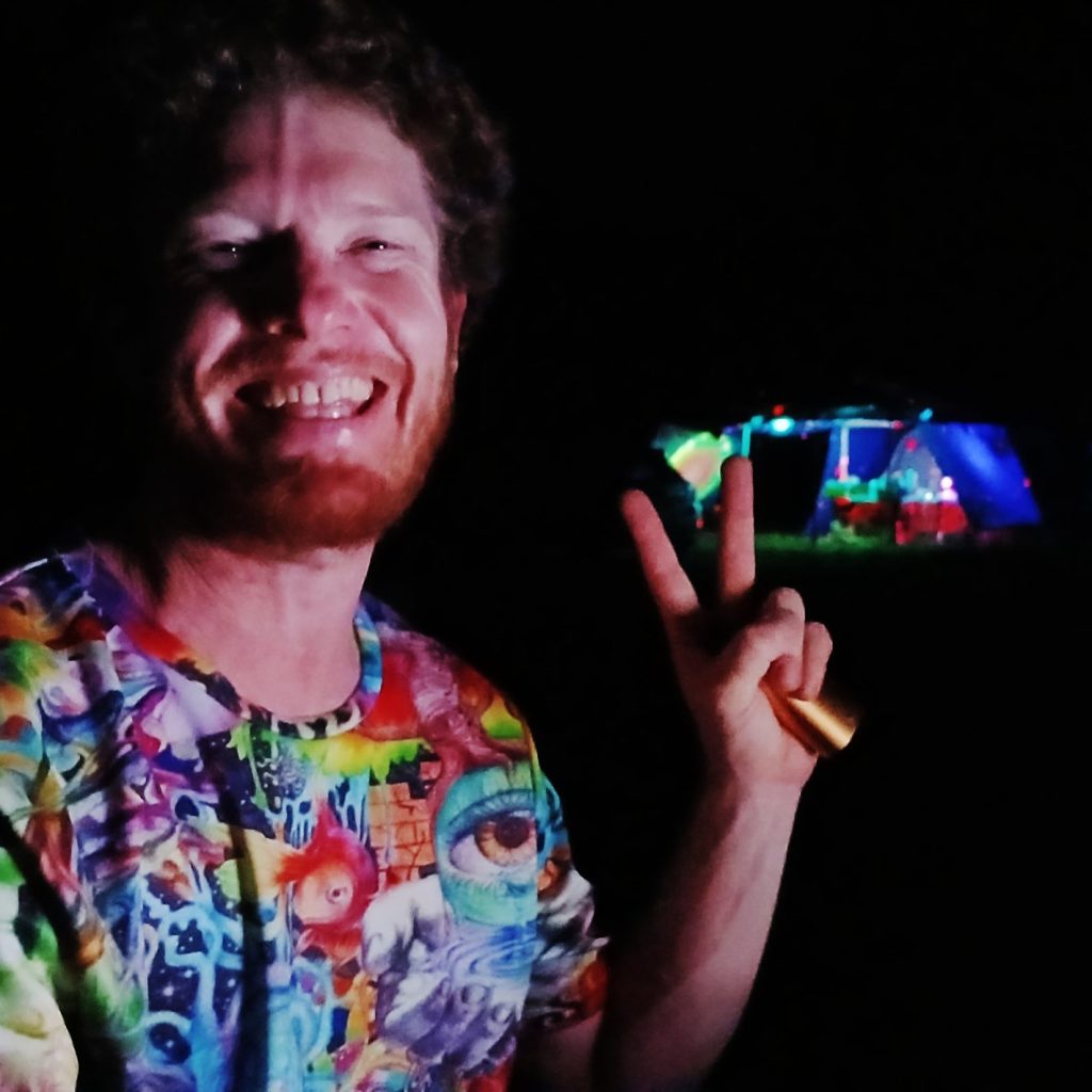 Man smiling, colourful shirt, peace sign, night background.