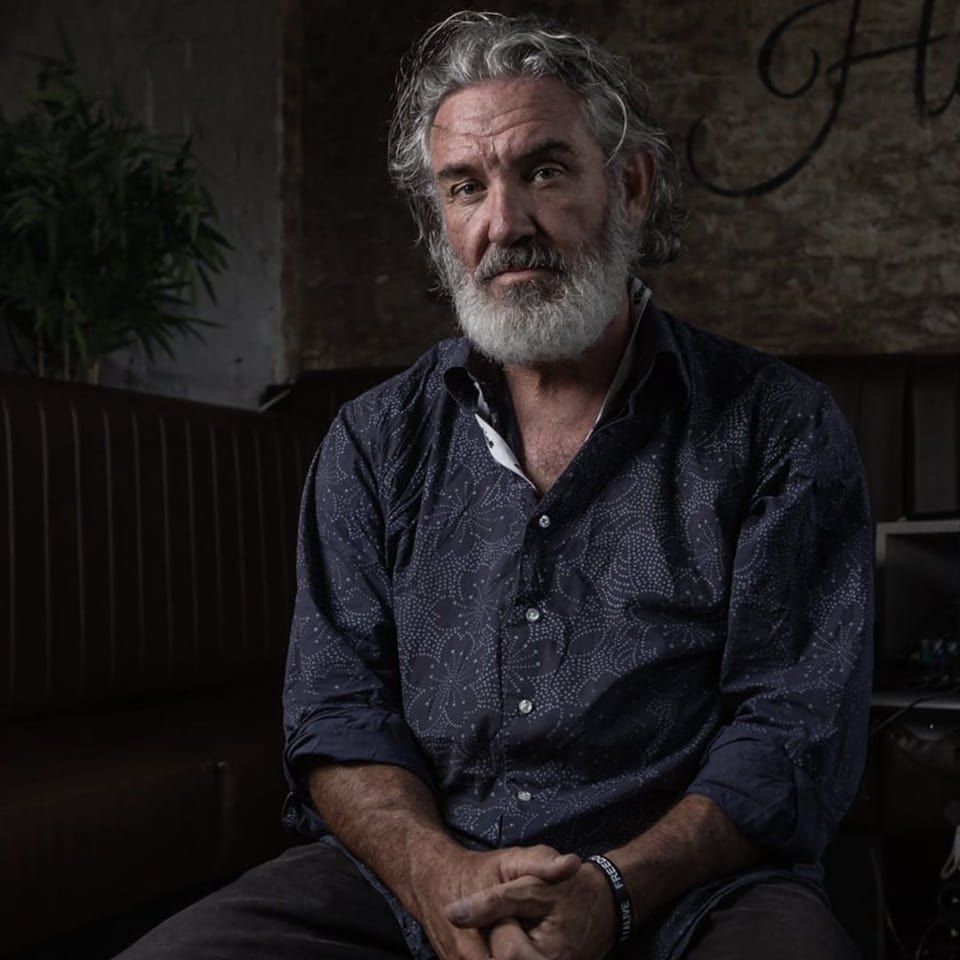 Man with grey beard sitting indoors.