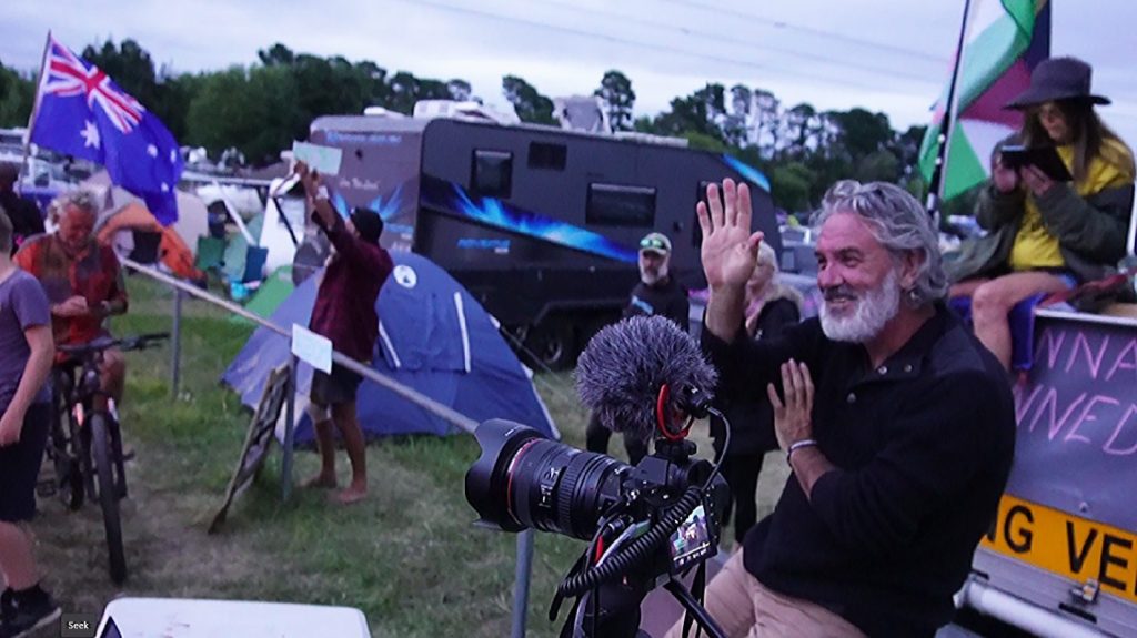 Man with camera at outdoor event, Australian flags visible.